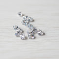 Several small clear faceted zircon beads scattered on a light brown wood-grain surface.