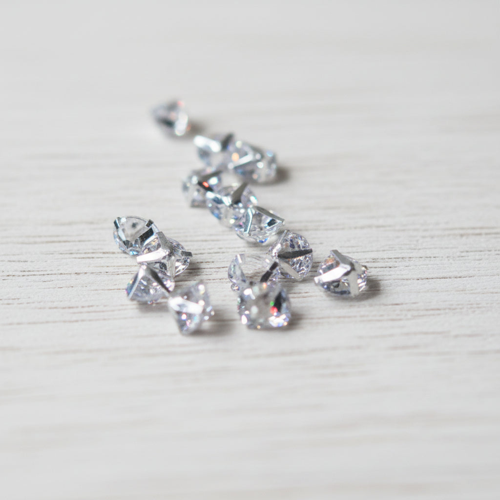 Several small clear faceted zircon beads scattered on a light brown wood-grain surface.