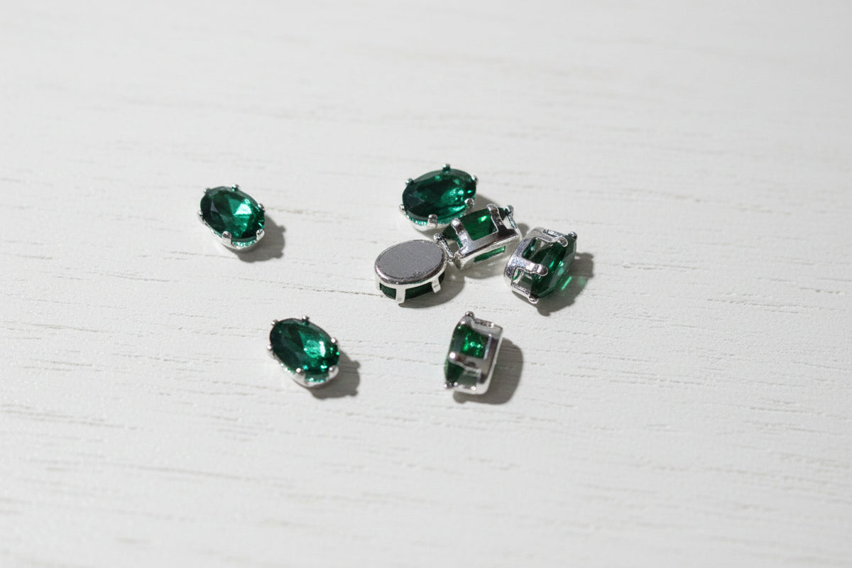 green zircon bead in silver settings arranged on a light wood grain surface.