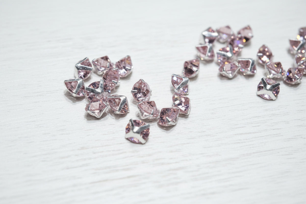 Several faceted pink iridescent zircon beads with silver prong settings scattered on a light brown wood grain surface.