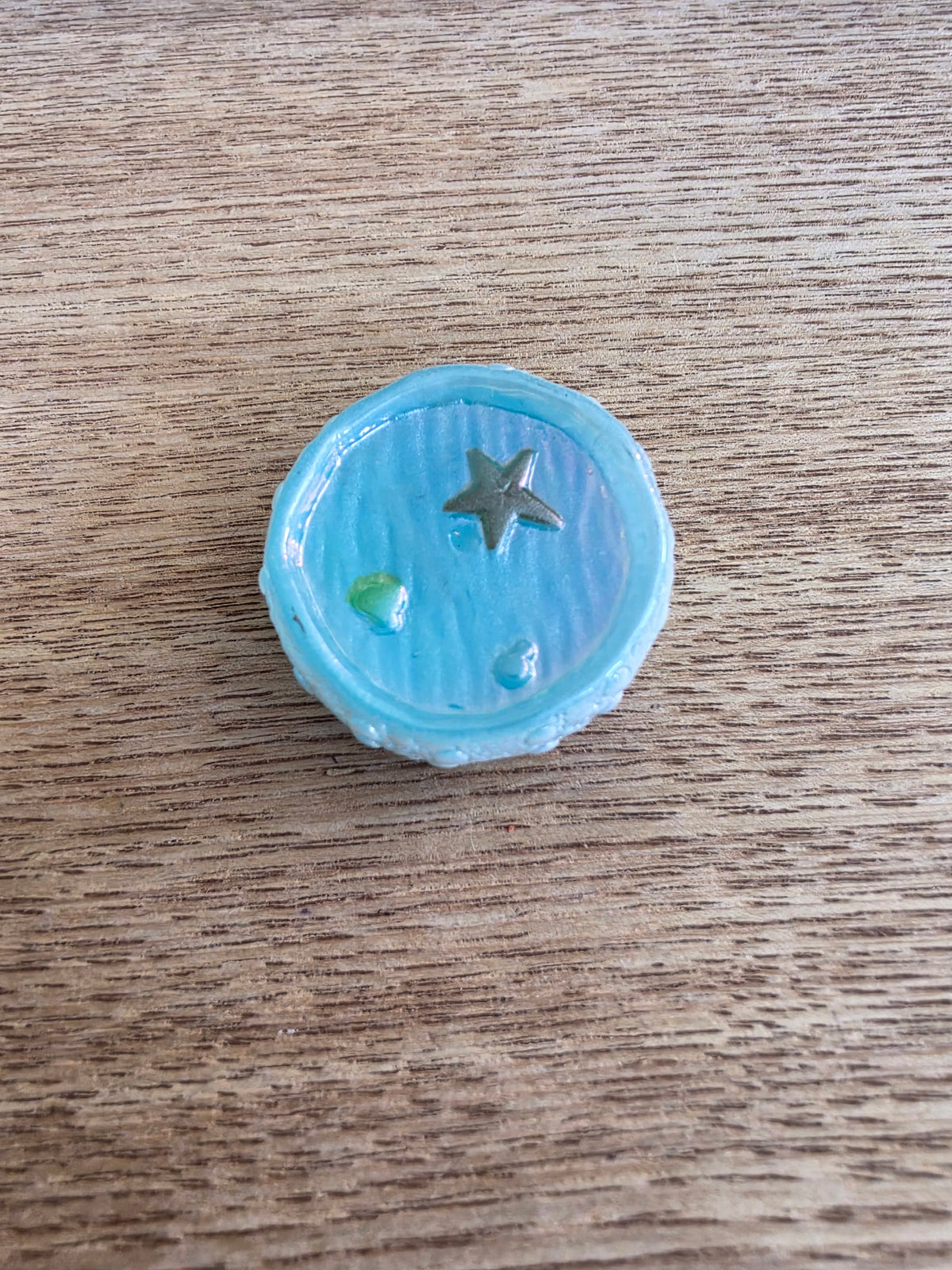 A small round light blue button with a metallic silver star in the center, resting on a brown wooden surface.