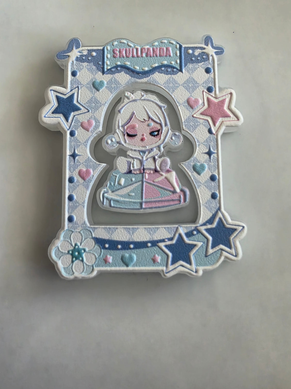 An acrylic bead set featuring a stylized anime character with closed eyes, pale blue hair, and a pastel dress in blue, pink, and white. The piece has embossed star, heart, and floral details, with the word 'SKULLPANDA' at the top, photographed on a plain light gray surface.