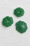 Three green lily pad-shaped decorative pieces arranged on a plain white surface.