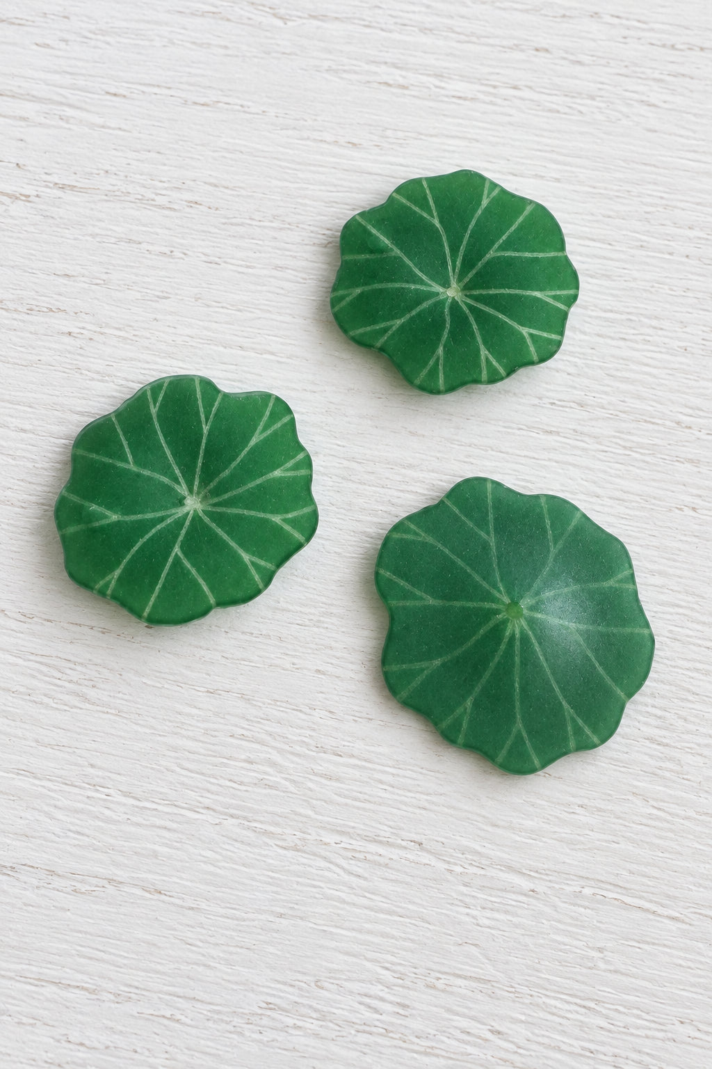 Three green lily pad-shaped decorative pieces arranged on a plain white surface.