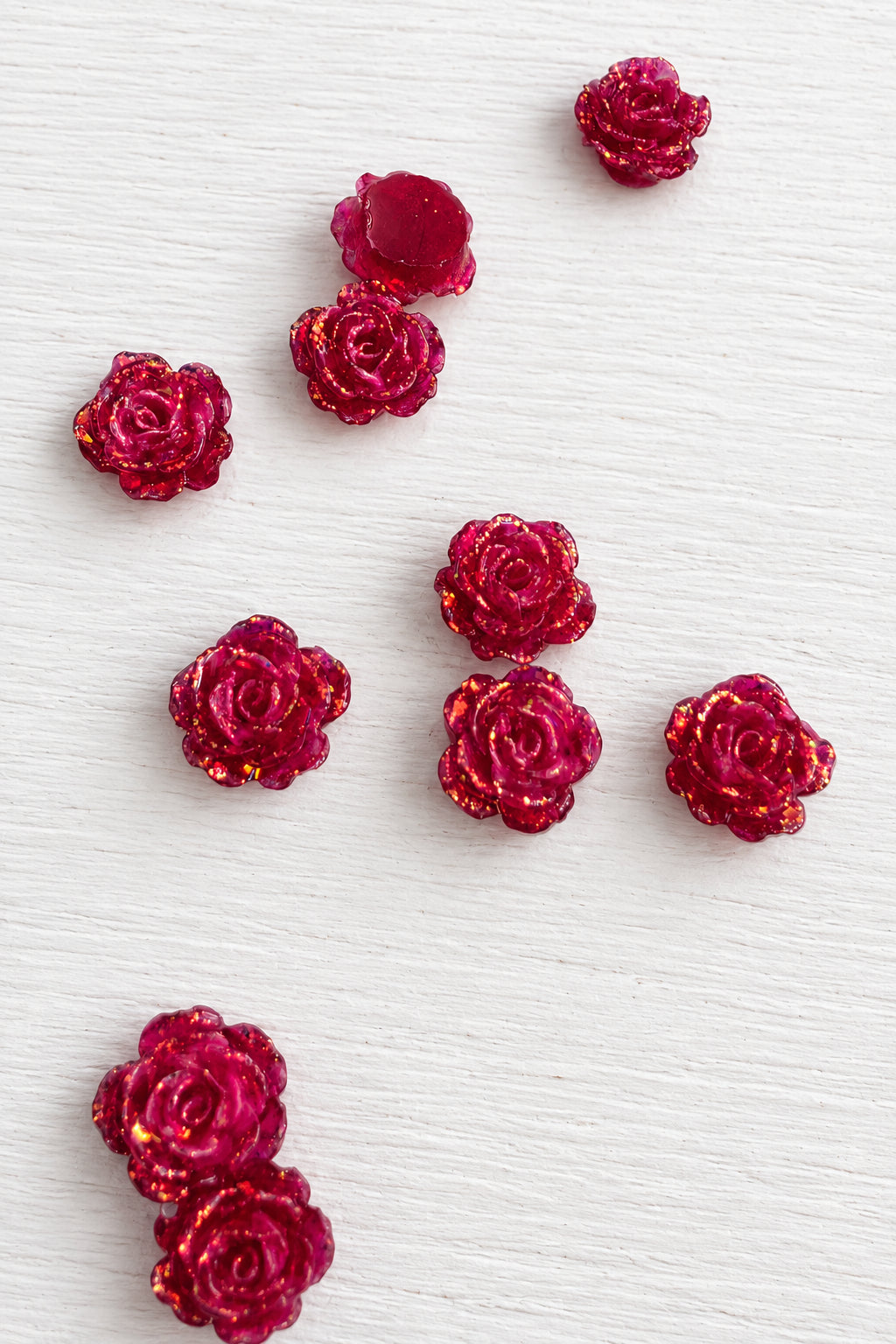Several small glittery red rose-shaped embellishments scattered on a plain white surface.