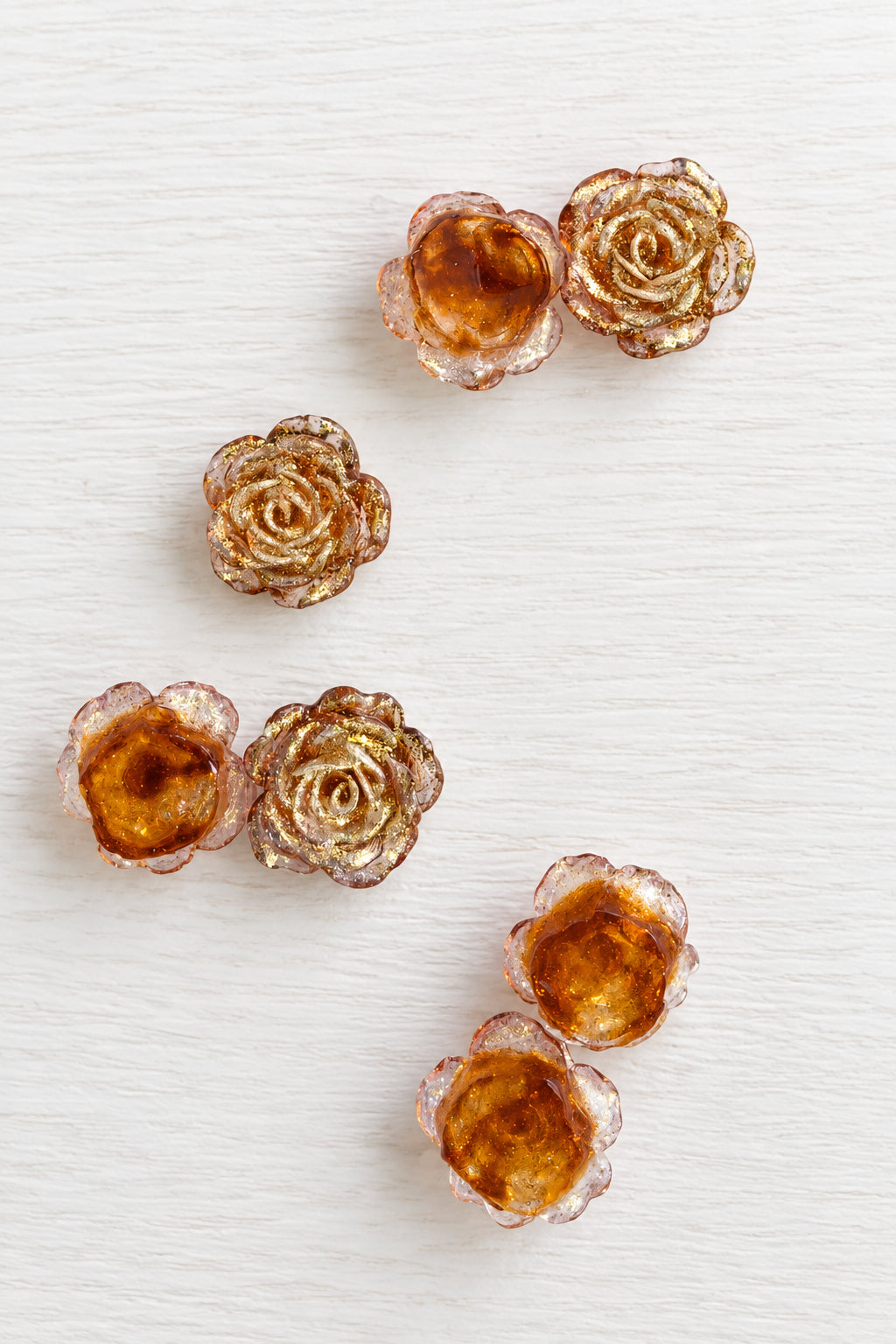 Small rose-shaped craft beads with metallic rose gold petals and amber-coloured centres.