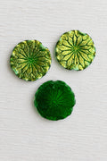 Round textured green and gold leaf-shaped decorative pieces arranged on a plain white background.
