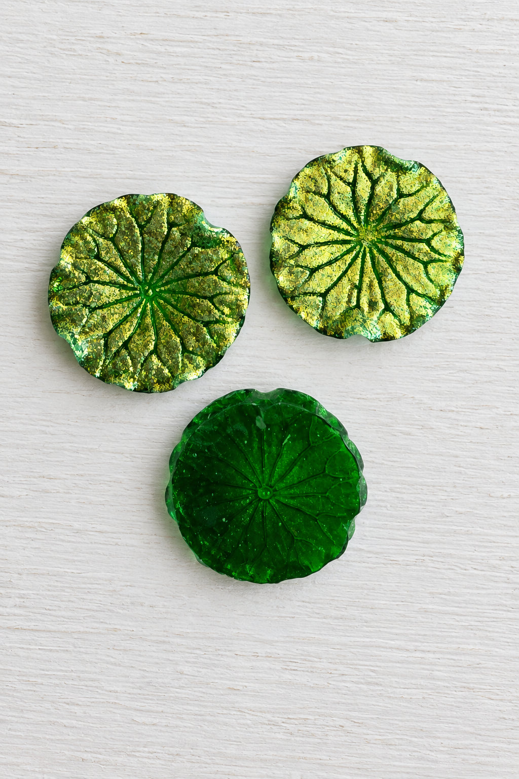Round textured green and gold leaf-shaped decorative pieces arranged on a plain white background.