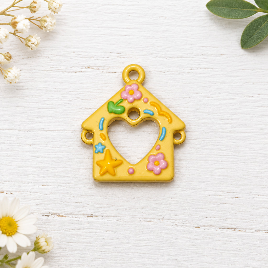 A small yellow house-shaped charm with a heart cut out in the centre, decorated with pastel pink flowers, a green leaf, and colourful stars.