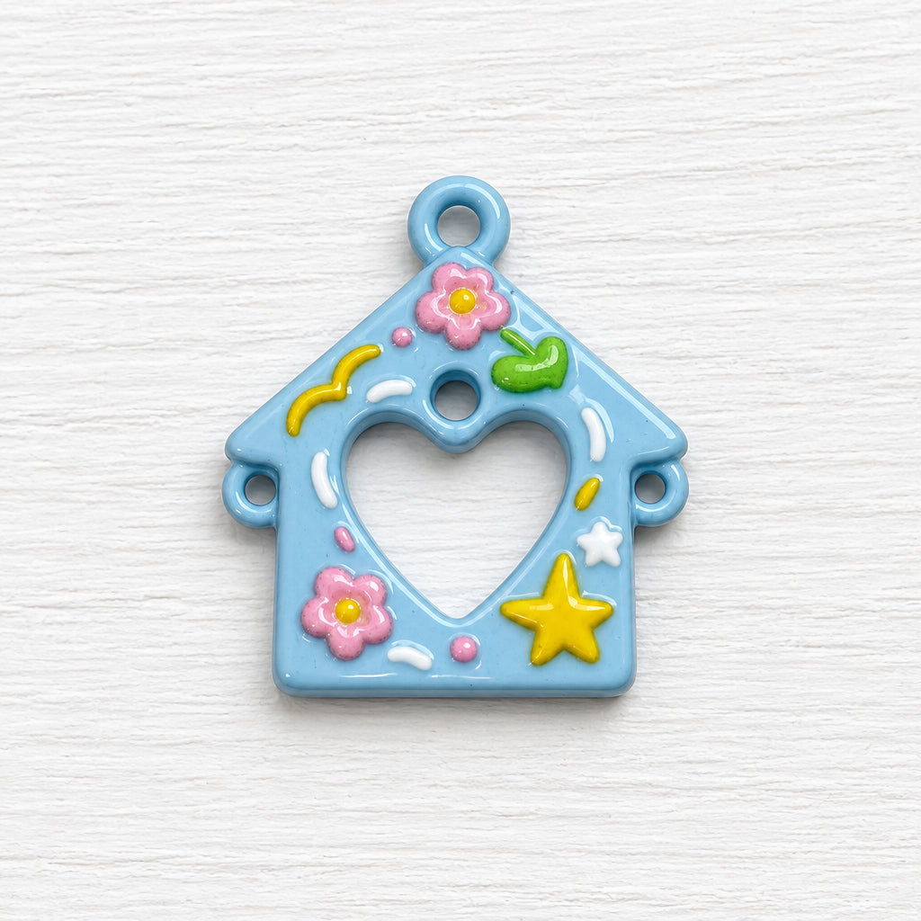 A small light blue house-shaped charm with a heart cut out, decorated with pink flowers, a yellow star, and small green and pink accents.