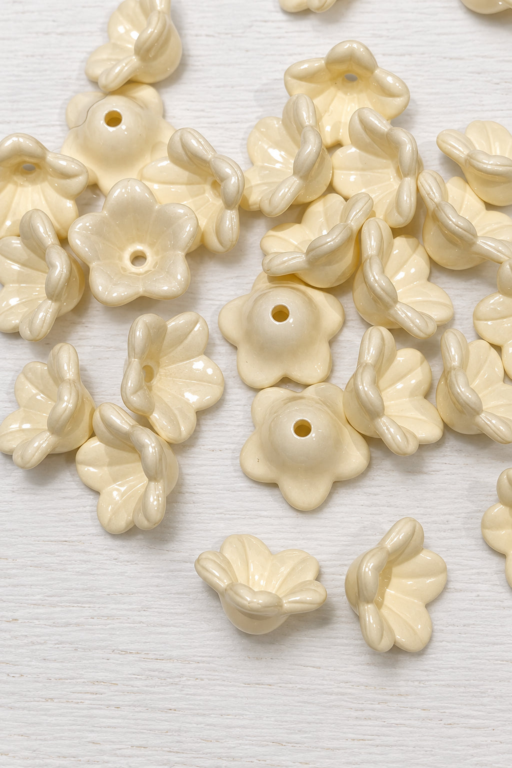 A pile of glossy cream-coloured acrylic flower shaped beads with a central hole, arranged on a light surface.