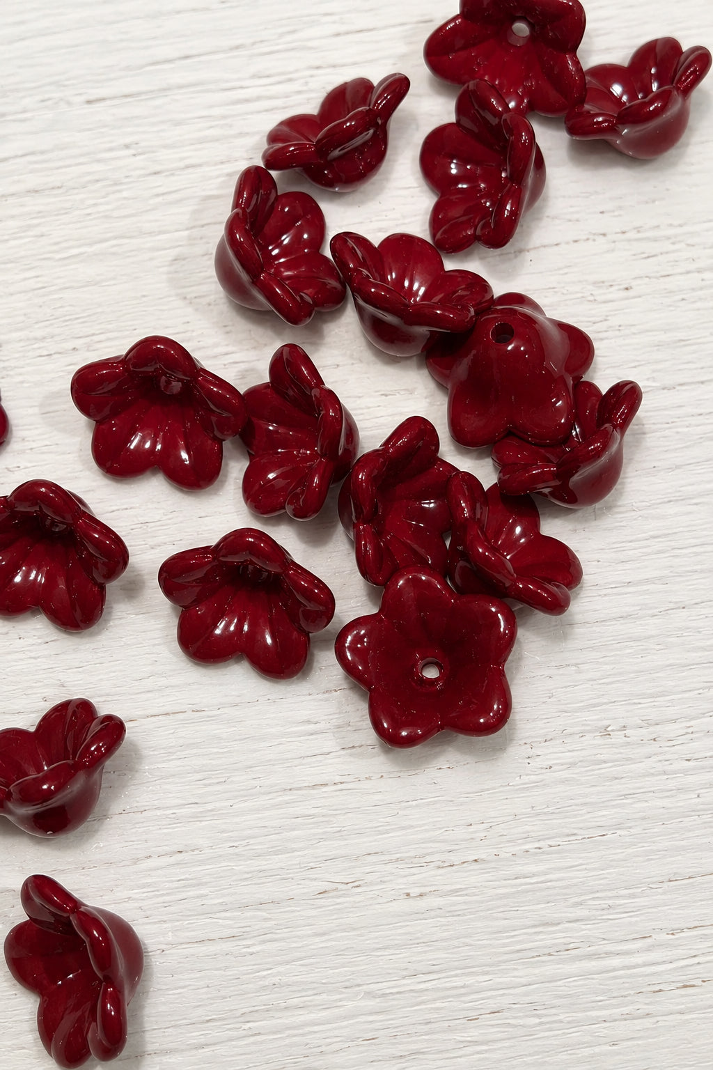 Several glossy dark red flower-shaped beads scattered on a white surface.