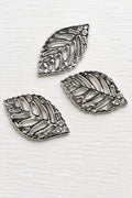 Acrylic silver leaf-shaped pendants with detailed cut out leaf patterns, displayed on a glossy white surface.