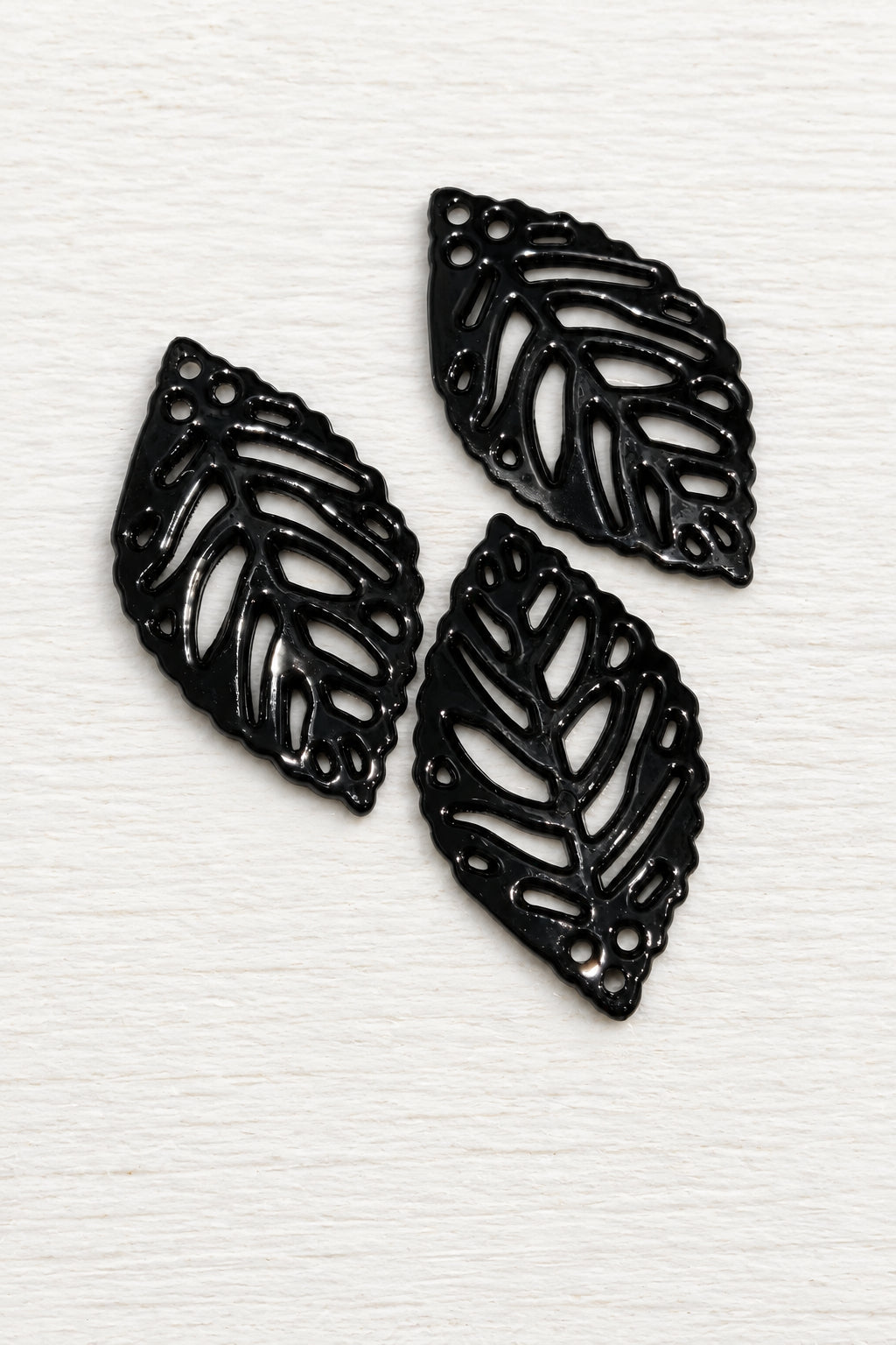 Acrylic black leaf-shaped pendants with cut out leaf patterns, displayed on a white surface.