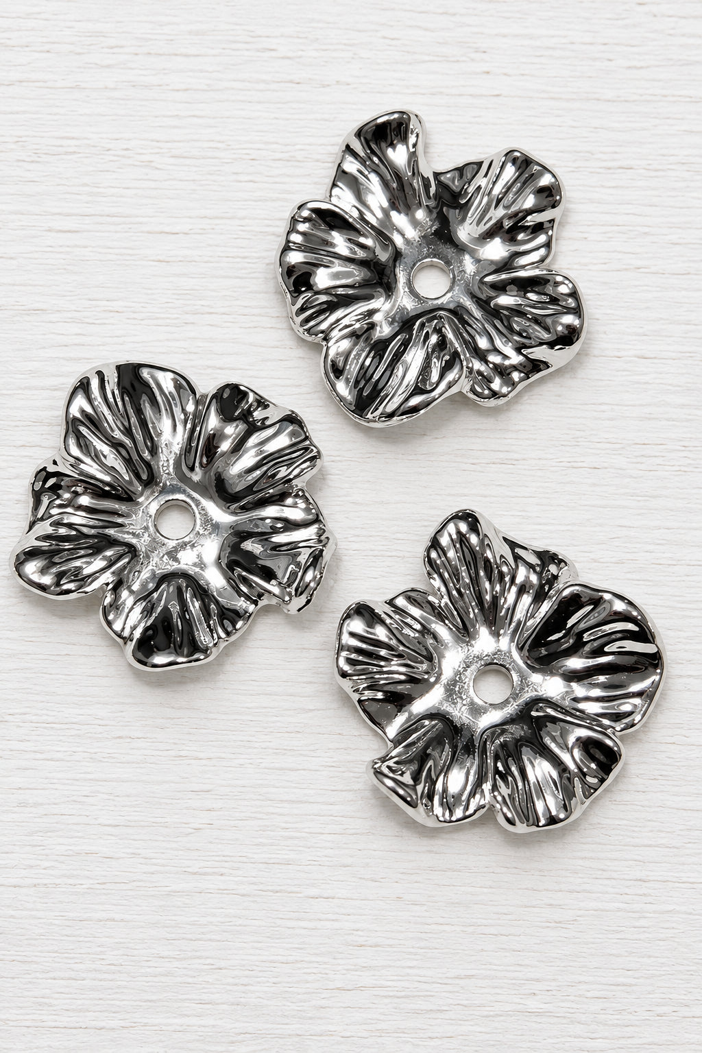 Shiny acrylic silver coloured flower-shaped beads with a textured, ribbed petal design, arranged on a white surface.