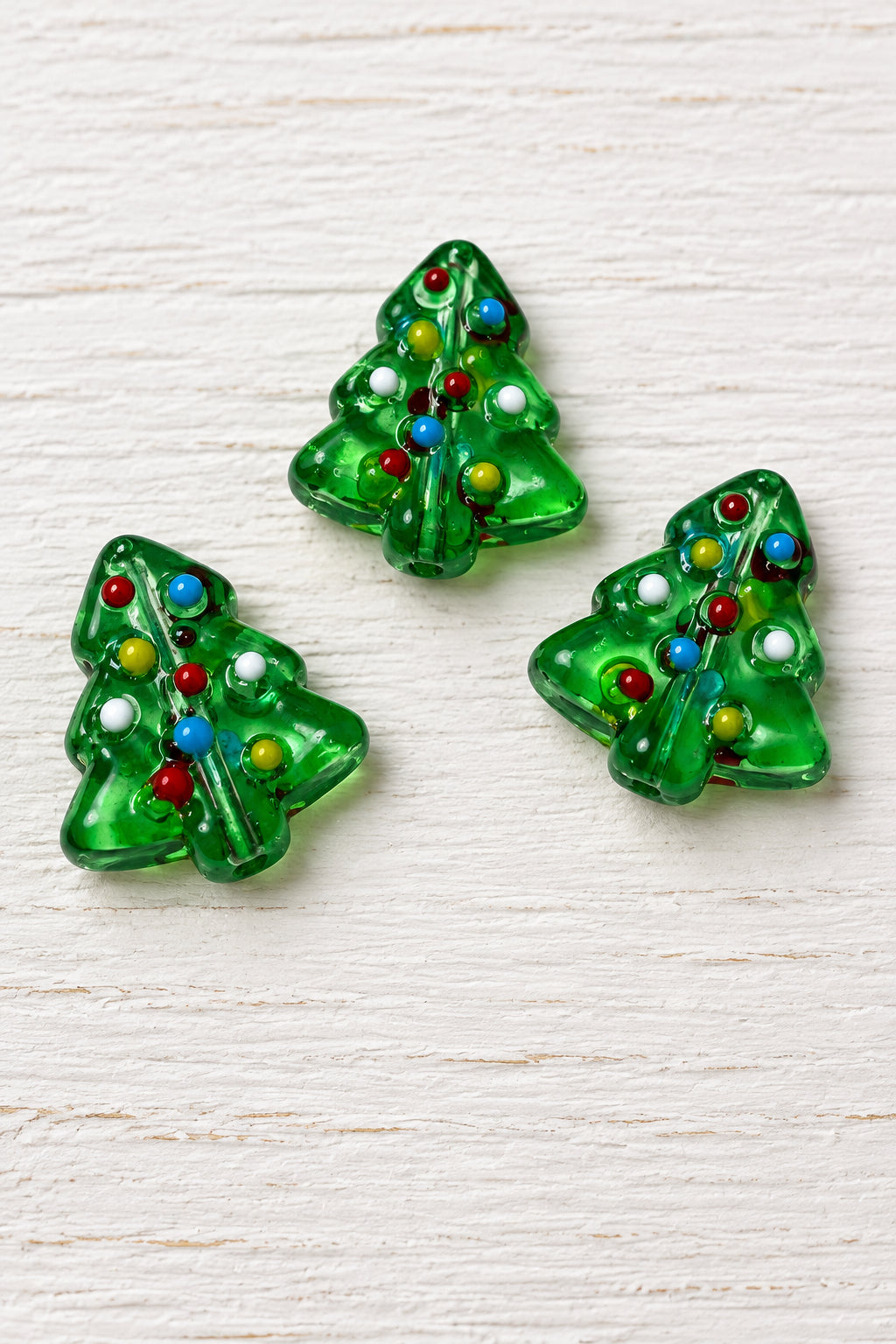 Small green glass Christmas tree-shaped  bead with multicoloured dot details, arranged on a plain white surface.