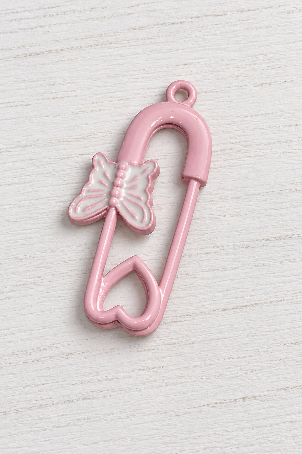 A pink safety pin charm with a heart-shaped bottom and a butterfly accent on the side.