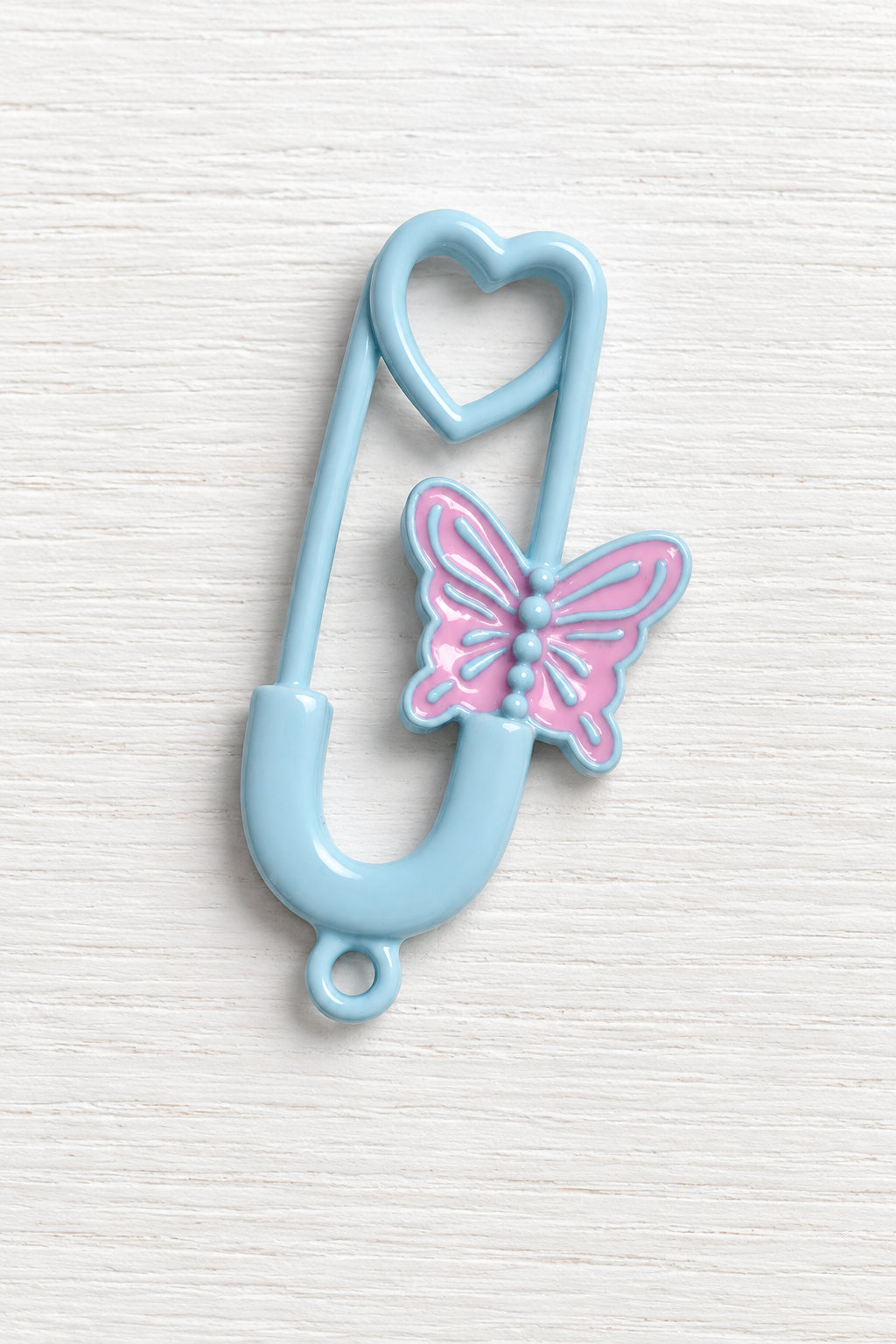 A light blue safety pin-shaped hair clip with a pink butterfly charm in the centre.