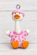 A small duck-shaped pendants. The duck has a white body, orange beak and feet, and wears a pink hat and pink outfit with orange polka dots.
