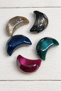 Five glossy crescent-shaped beads in assorted colours and finishes, including smoky brown, black, navy blue, emerald green, and magenta.