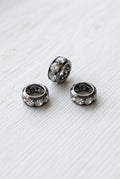Gunmetal spacer beads, each set with clear rhinestones, displayed on a white surface.