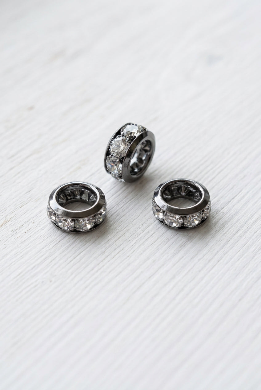 Gunmetal spacer beads, each set with clear rhinestones, displayed on a white surface.