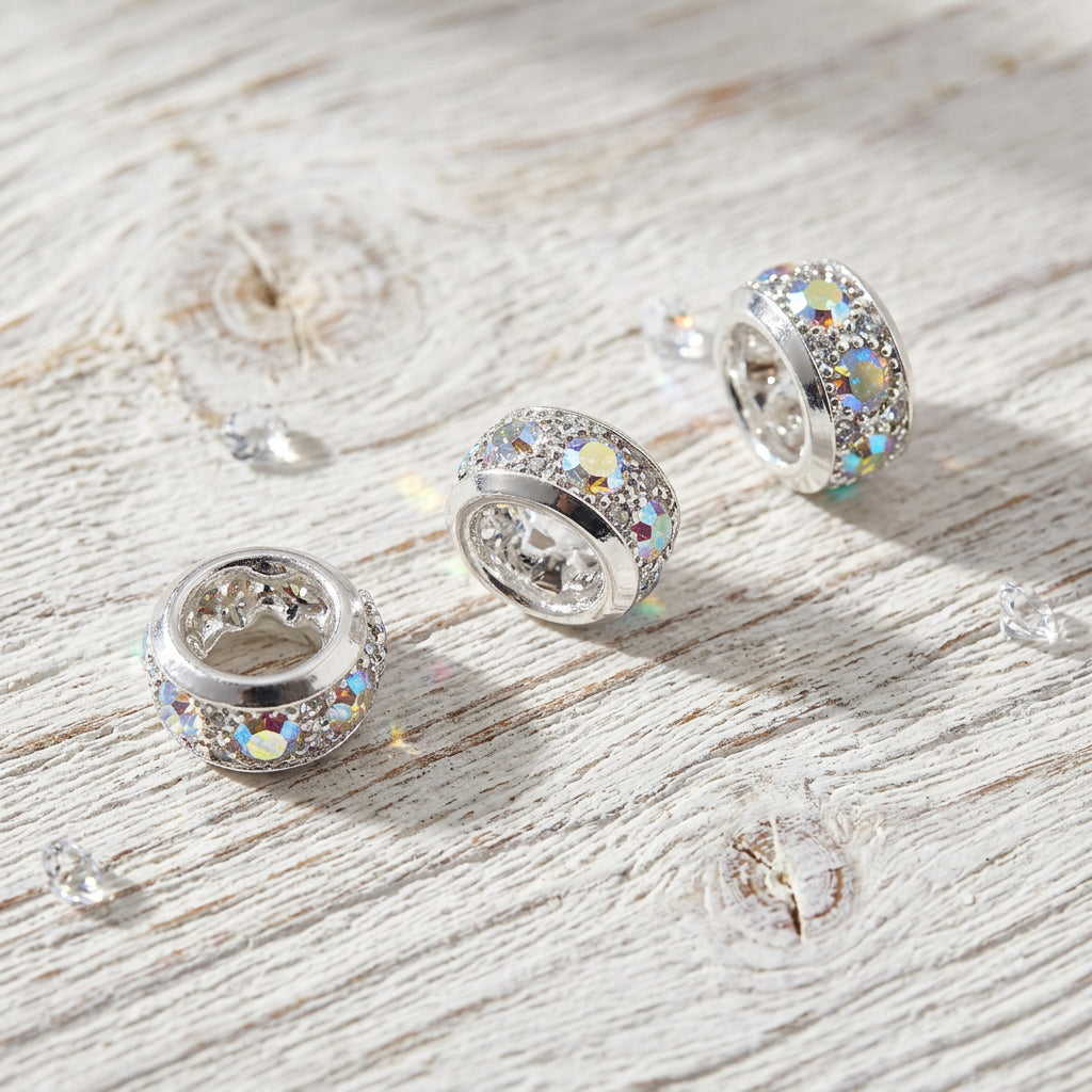 Silver-toned spacer beads with sparkling clear stones, arranged on a white surface.