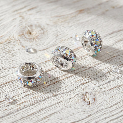 Silver-toned spacer beads with sparkling clear stones, arranged on a white surface.