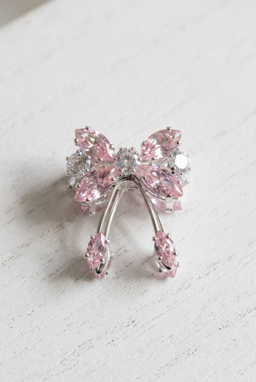 A silver-toned bow-shaped bead embellished with pink marquise-cut and clear round zircons, displayed on a white surface.