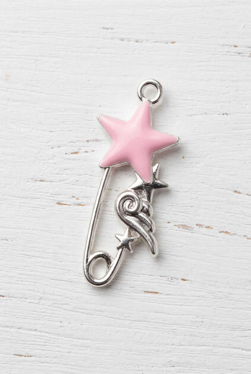 A silver safety pin charm shaped like a wand, featuring a pink star on the handle and a small silver bird detail, shown on a plain white surface.