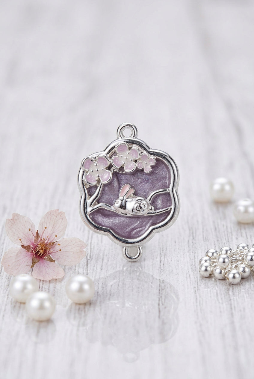 A silver-toned metal charm with a lavender-purple enamel background, featuring a cherry blossom design and a small central silver charm, shown on a plain light surface.