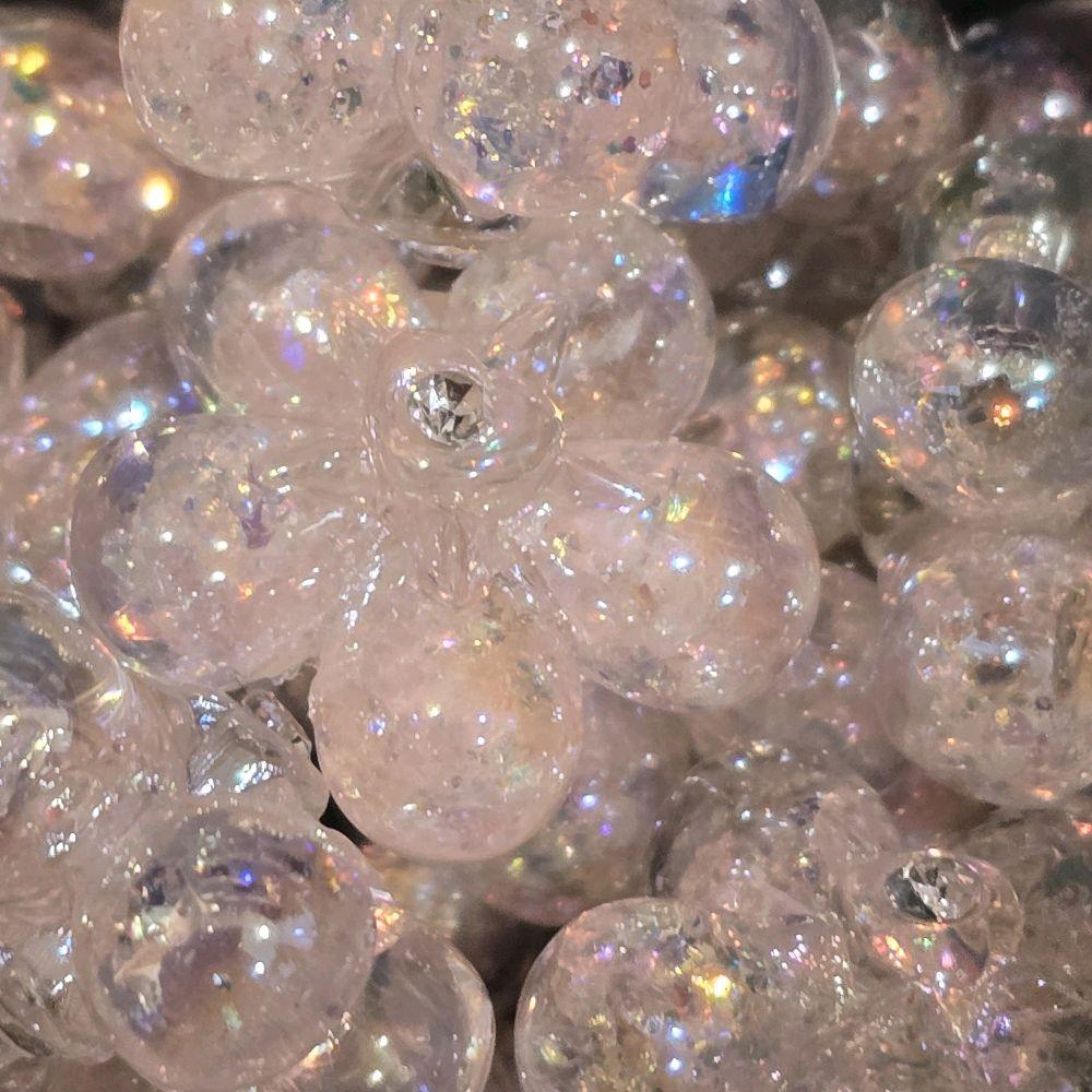 A close-up pile of pink, flower-shaped beads filled with iridescent glitter and small rhinestones in the center.