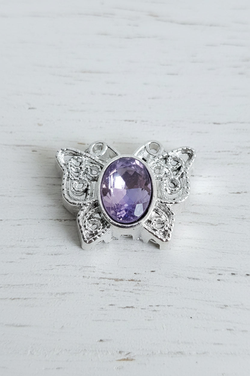A silver-toned filigree multi hole bead featuring a purple glass crystal in the centre