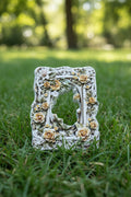An ornate rectangular decorative frame acrylic bead with a floral pattern in cream, yellow, and green on a white background