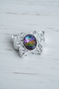 A silver-toned filigree bead featuring a prominent oval-cut galaxy glass crystal in the center.